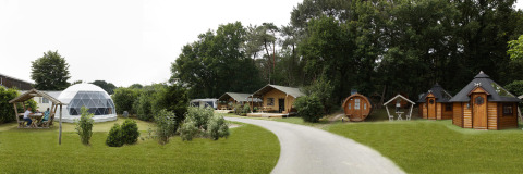 Panoramisch zicht op Safari tent lodge met koepel, houten huisjes en omliggend groen landschap.