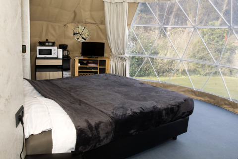 Interior view of Dome at Costa Kabrita in the Netherlands, featuring a bed, TV, and panoramic windows.