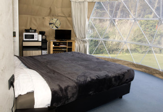 Interior view of Dome at Costa Kabrita in the Netherlands, featuring a bed, TV, and panoramic windows.