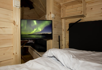 Interior de la tiny house Finse Kota en Costa Kabrita, Países Bajos, con cama y televisor con auroras boreales.