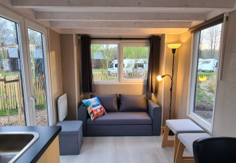 Lys stue i et tiny house på Vakantiepark 't Urkerbos, Holland, med sofa, store vinduer og udsigt udenfor.