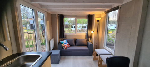 Salon lumineux d'une tiny house au Vakantiepark 't Urkerbos, Pays-Bas, avec canapé, grandes fenêtres et vue extérieure.