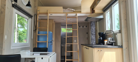 Interior de tiny house con altillo, cocina, mesa de comedor y ventanas grandes, en los Países Bajos.