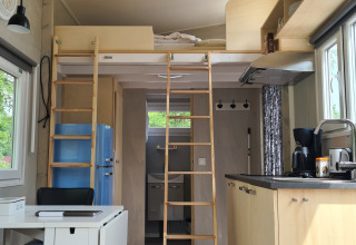 Interior de tiny house con altillo, cocina, mesa de comedor y ventanas grandes, en los Países Bajos.