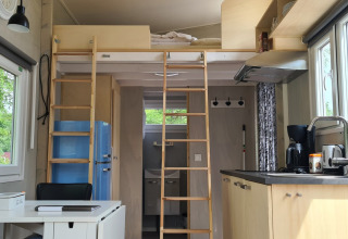 Interior de tiny house con altillo, cocina, mesa de comedor y ventanas grandes, en los Países Bajos.