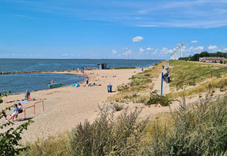 Strand aan Vakantiepark 't Urkerbos, Flevoland met mensen, zee, strand en windmolens op de achtergrond.