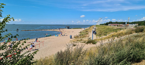 Strand aan Vakantiepark 't Urkerbos, Flevoland met mensen, zee, strand en windmolens op de achtergrond.