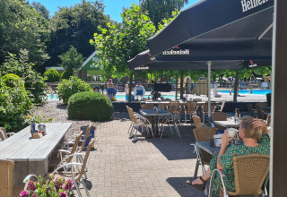 Zonnig buitenterras met zicht op het zwembad bij Vakantiepark 't Urkerbos, Flevoland, Nederland.