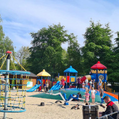 Niños juegan en un colorido parque infantil en Vakantiepark 't Urkerbos, rodeados de árboles y familias.