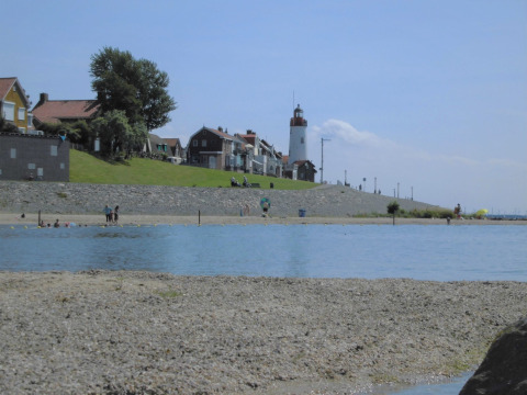 Strand med udsigt til en fyrtårn og huse i baggrunden ved Vakantiepark 't Urkerbos i Flevoland, Holland.