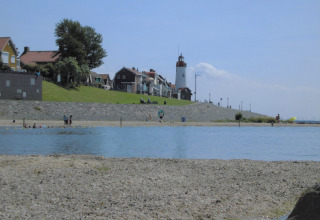 Strandzicht met vuurtoren en huizen op de achtergrond bij Vakantiepark 't Urkerbos, Flevoland, Nederland.