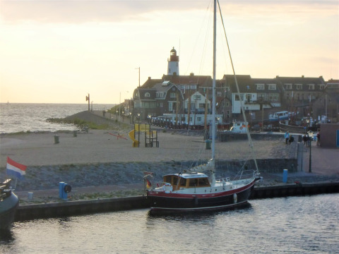 Barca a vela attraccata al porto vicino a Urk, Flevoland, Paesi Bassi, con faro e villaggio sullo sfondo.