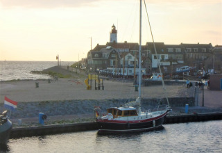 Zeilboot aangemeerd aan de haven bij Urk, Flevoland, Nederland, met vuurtoren en huizen op de achtergrond.