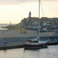 Velero atracado en el puerto cerca de Urk, Flevoland, Países Bajos, con faro y casas de pueblo al fondo.