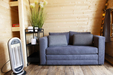 Modern living space in Glamping Pod at Costa Kabrita, Netherlands, with cozy grey sofa and heater.