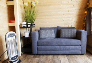 Modern living space in Glamping Pod at Costa Kabrita, Netherlands, with cozy grey sofa and heater.