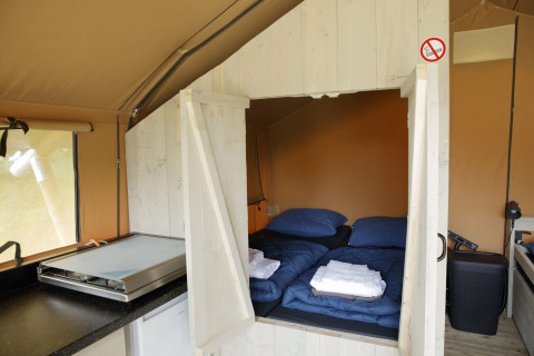 Interior of a Safari tent at Costa Kabrita in the Netherlands showing beds with linens and a small kitchen.