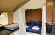 Interior of a Safari tent at Costa Kabrita in the Netherlands showing beds with linens and a small kitchen.