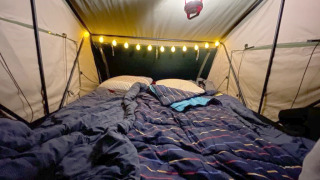 Cozy tent interior with bed, string lights, and lantern at Treelodge treehouse at Costa Kabrita, Netherlands.