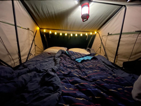 Indretning af et hyggeligt telt med seng, puder og lyskæde i træhuset Treelodge ved Costa Kabrita, Holland.