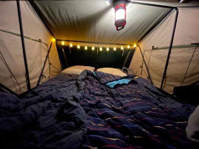 Interior de tienda acogedora con cama, luces y linterna en Treelodge en Costa Kabrita, Países Bajos.