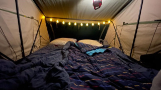 Interior de tienda acogedora con cama, luces y linterna en Treelodge en Costa Kabrita, Países Bajos.