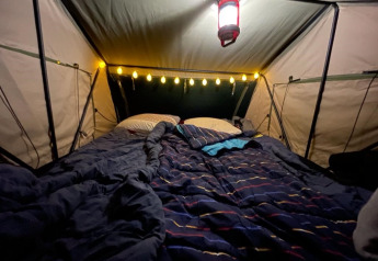 Gemütliches Zelt mit Bett, Lichterkette und Lampe im Baumhaus Treelodge bei Costa Kabrita in den Niederlanden.