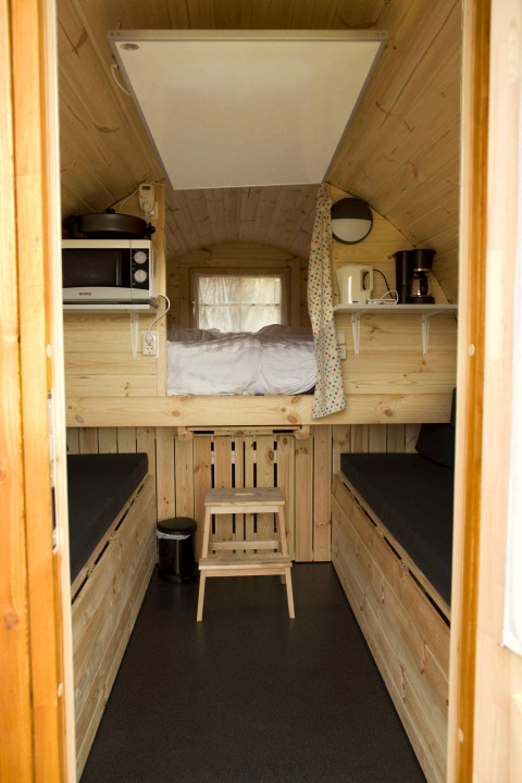 Intérieur d'une tiny house boisée avec lit mezzanine, banquettes et coin cuisine au Wijnvat, Costa Kabrita.