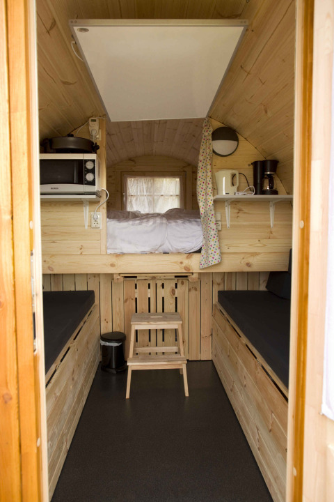 Tiny wooden house interior with loft bed, black benches, microwave, and coffee maker at Costa Kabrita.