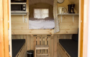 Interno di una tiny house in legno con letto rialzato, panche nere e cucina al Wijnvat, Costa Kabrita.