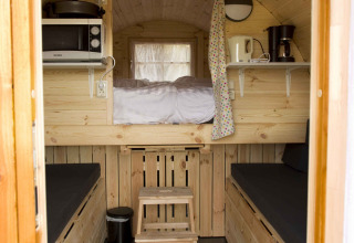 Interior de casa pequeña de madera con cama tipo altillo, sillones y cocina en Wijnvat, Costa Kabrita.
