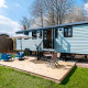 Shepherd Lodge glamping, udendørs siddeområde med paraply, trædæk, blå vogn og grøn græsplæne.