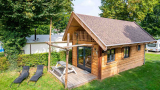 Tiny wooden house named Jachthut at Camping Vinkenhof, Netherlands, with patio, picnic table, and loungers.