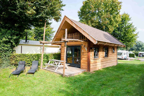 Tiny house Jachthut with porch and lounge chairs at Camping Vinkenhof, surrounded by greenery in the Netherlands.