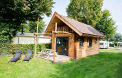 Tiny house Jachthut with porch and lounge chairs at Camping Vinkenhof, surrounded by greenery in the Netherlands.