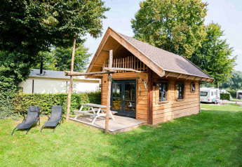 Casa pequeña Jachthut con porche y sillas de jardín en Camping Vinkenhof, rodeada de naturaleza en Países Bajos.