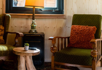 Acogedor rincón en la tiny house Jachthut de Camping Vinkenhof, con sillones verdes y mesa rústica de madera.