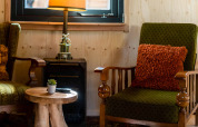 Cozy sitting area in Jachthut tiny house at Camping Vinkenhof, with green chairs, rustic table, and warm lamp.