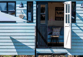 Alojamiento glamping Shepperd Lodge de color azul con puerta abierta, escaleras y área interior acogedora.