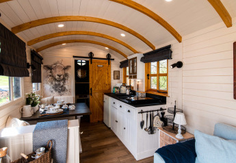 Cozy interior of Shepperd Lodge glamping, featuring wood arches, kitchen, dining area, and comfortable seating.