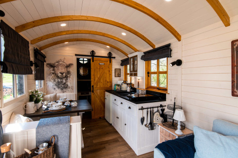 Cozy interior of Shepperd Lodge glamping, featuring wood arches, kitchen, dining area, and comfortable seating.