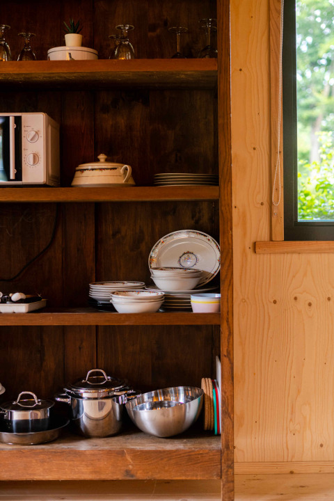Wooden kitchen shelf in Jachthut tiny house at Camping Vinkenhof, Netherlands, with cookware and dishes.