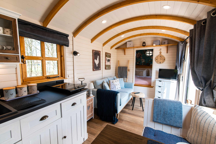 Acogedor alojamiento glamping Shepperd Lodge con interior de madera, cocina pequeña y zona de estar.