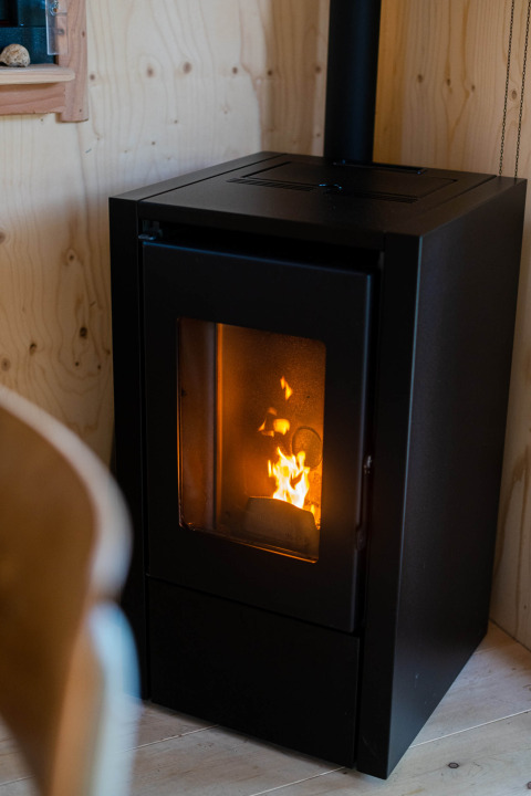 Black wood-burning stove with visible flames inside a tiny house at Camping Vinkenhof, Netherlands.