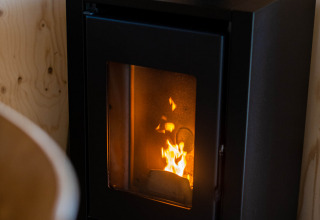 Sort brændeovn med flammer i et lille træhus på Camping Vinkenhof, Holland, fotograferet indendørs.