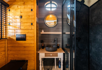 Baño moderno en Shepperd Lodge glamping con paredes de madera, espejo redondo y lavabo de piedra negra.