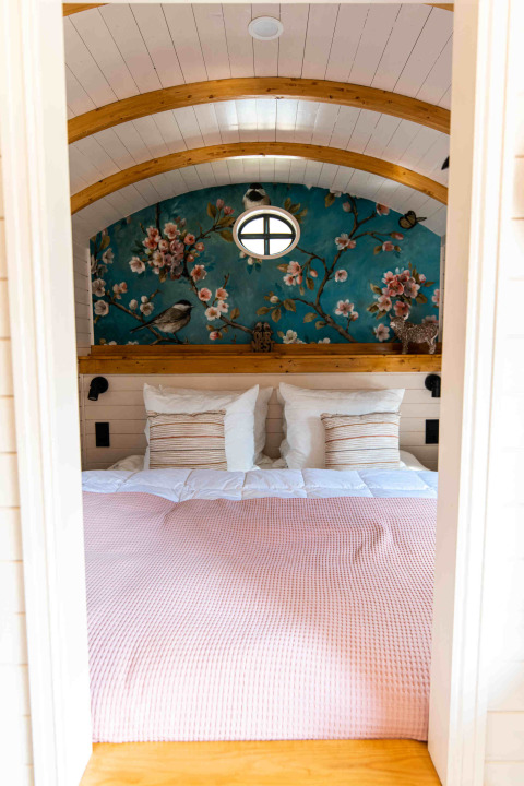 Zona notte accogliente alla Shepperd Lodge glamping con parete floreale e archi in legno sopra il letto.