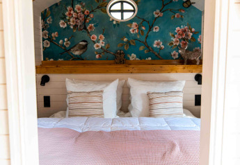 Zona notte accogliente alla Shepperd Lodge glamping con parete floreale e archi in legno sopra il letto.
