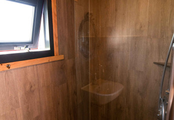 Modern shower in a tiny house at Jachthut, Camping Vinkenhof in the Netherlands, with wood-paneled walls.
