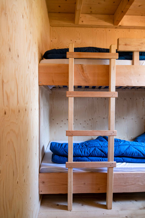 Ein Etagenbett aus Holz mit blauer Bettwäsche in einer kleinen Kabine in Jachthut, Camping Vinkenhof, Niederlande.